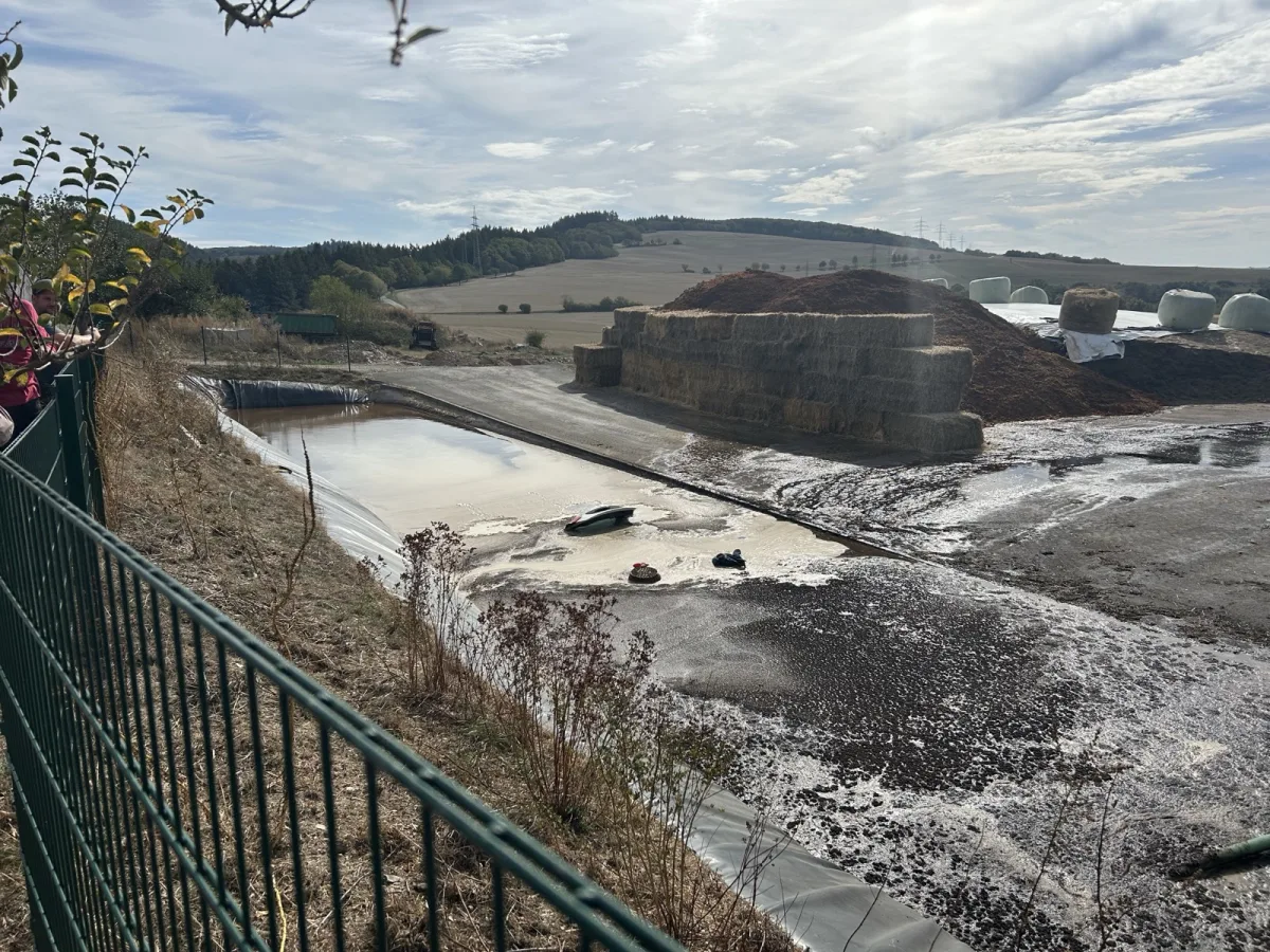 Ein Fahrzeug steckt in einem Wasserbecken fest, umgeben von landwirtschaftlichem Gelände und Heuballen.