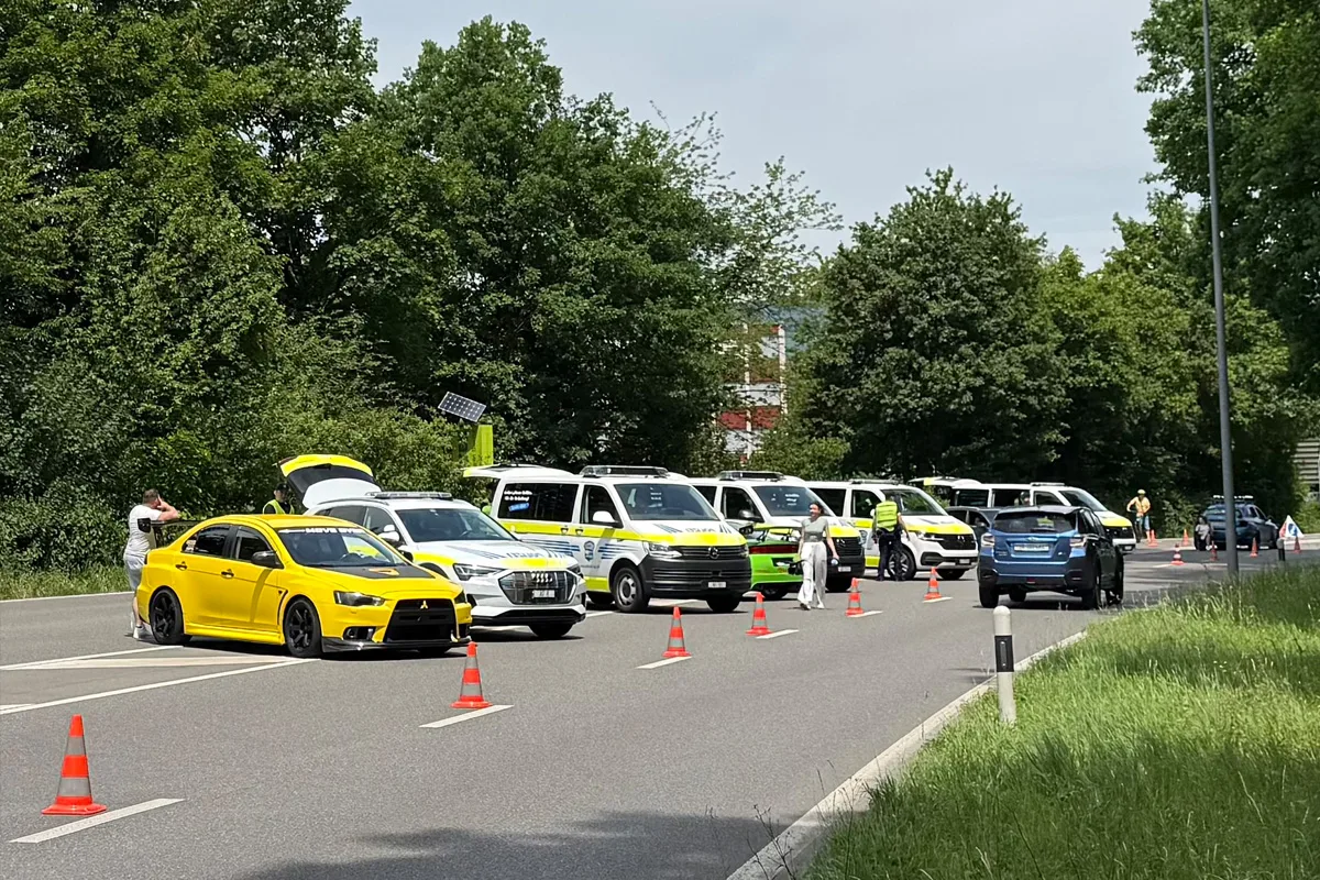 Mehrere Polizeifahrzeuge stehen geparkt auf einer Landstraße, daneben ein gelbes Auto mit offenem Kofferraum. Polizisten in Westen stehen in der Nähe.