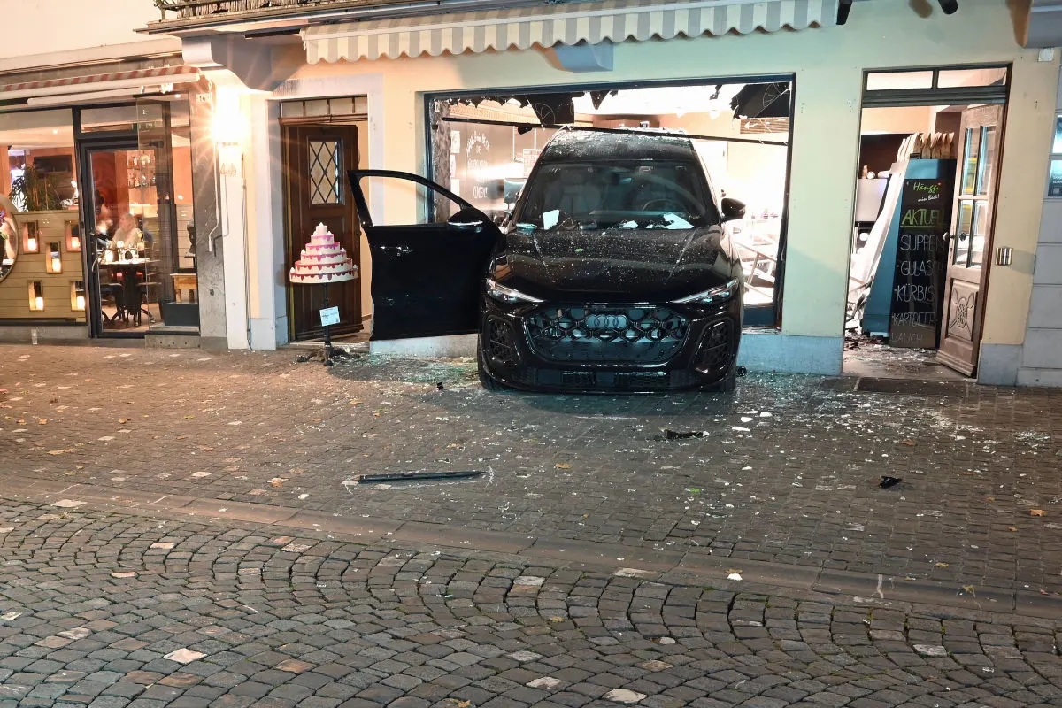 Ein schwarzes Fahrzeug, Modell Audi, steht mit eingeschlagenem Schaufenster in einem Ladengeschäft. Glasscherben sind verstreut.