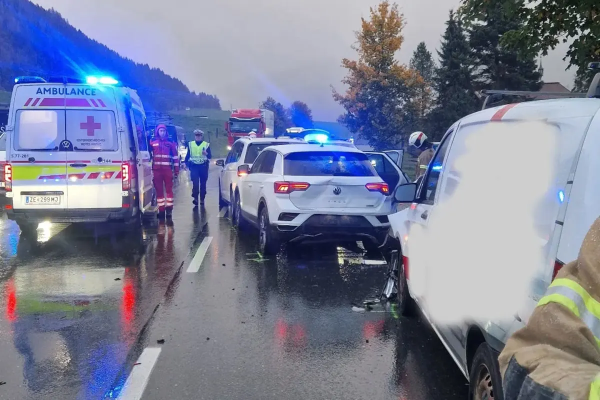 Ein Unfall auf einer regennassen Straße mit mehreren Einsatzfahrzeugen und Einsatzkräften der Rettung und Polizei.