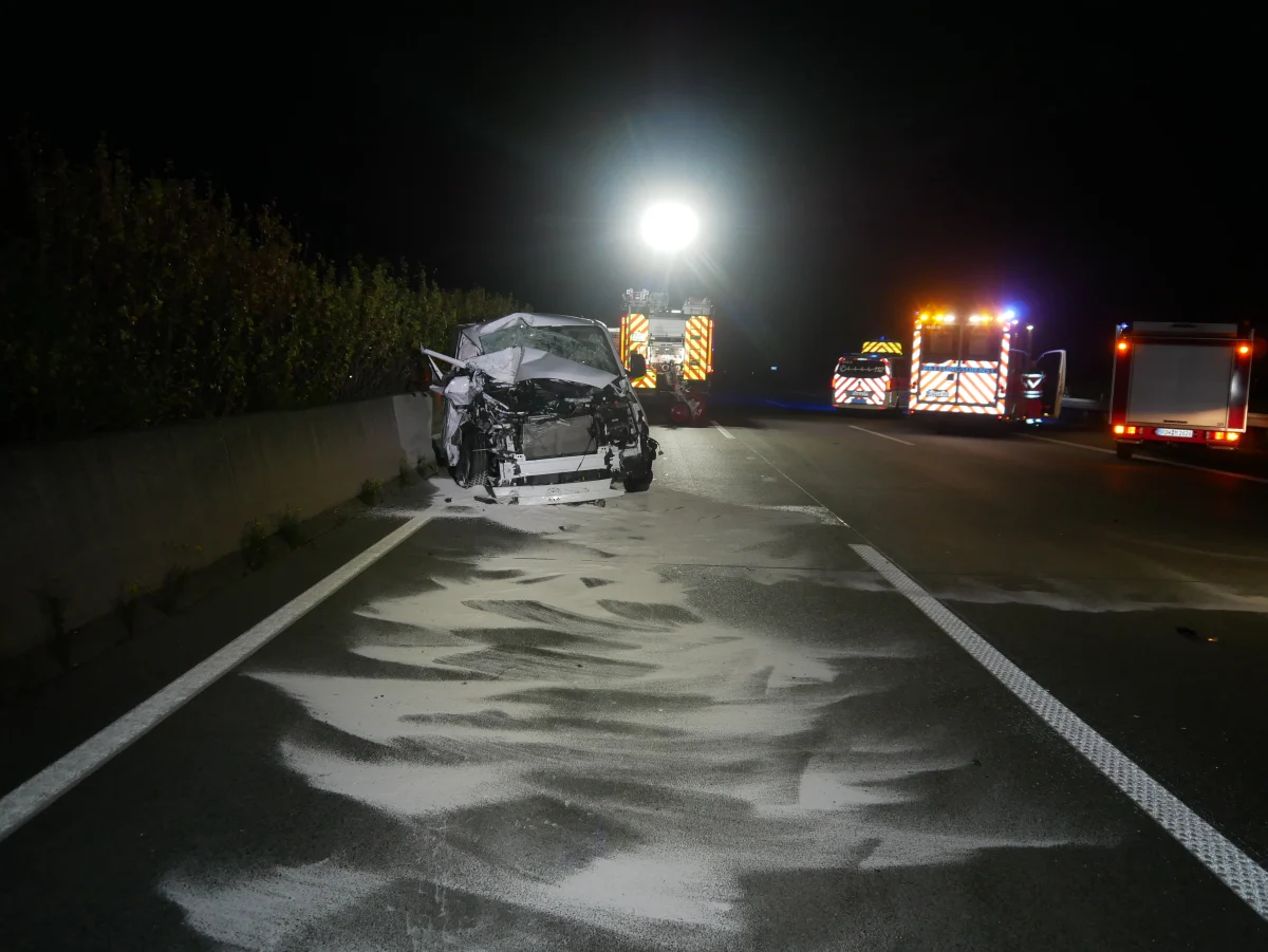 Ein stark beschädigter Pkw steht auf einer nächtlichen Autobahn, umgeben von mehreren Einsatzfahrzeugen mit aktivem Blaulicht.