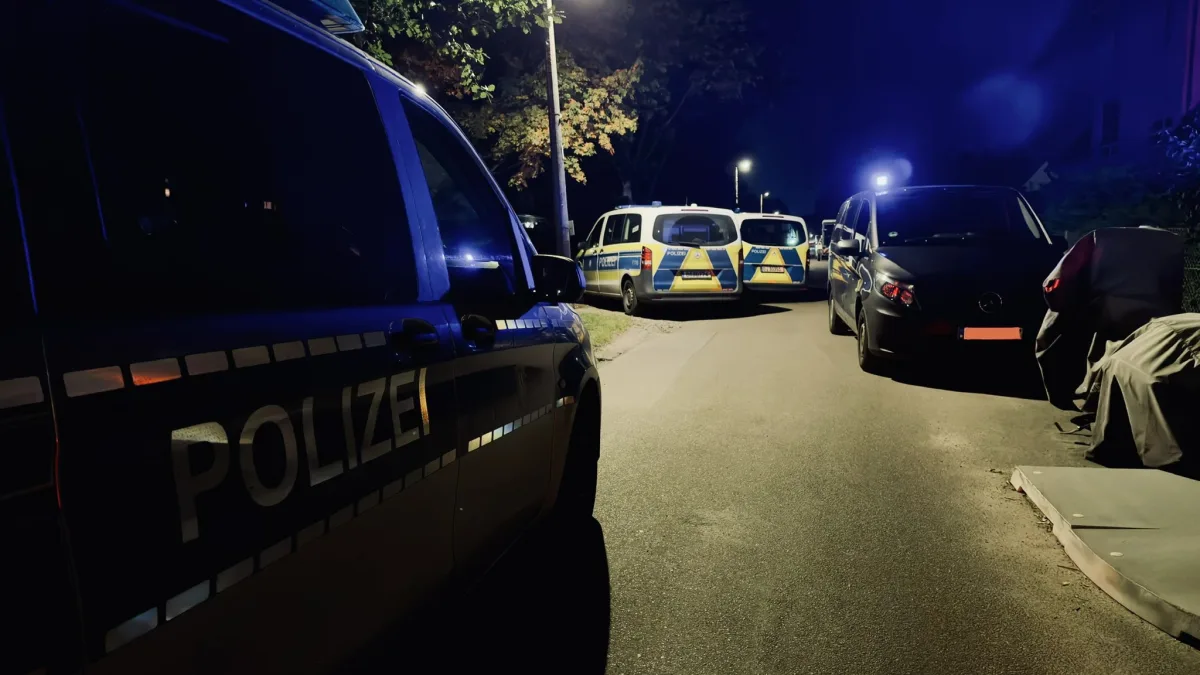 Mehrere Polizeifahrzeuge sind bei Nacht in einer Wohngegend geparkt und durch Straßenbeleuchtung beleuchtet.