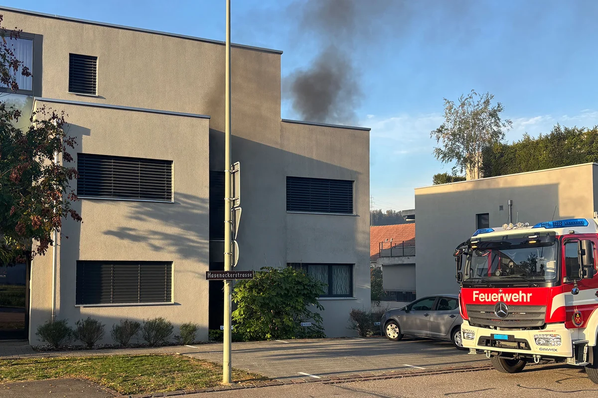 Ein Feuerwehrwagen steht vor einem modernen Wohngebäude, aus dem schwarzer Rauch aufsteigt.