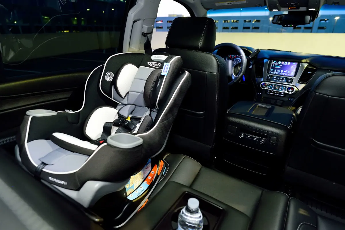 Ein Kindersitz ist auf der Rückbank eines Autos befestigt, umgeben von dunklen Sitzen. Das Auto steht in einem Parkhaus bei Nacht.