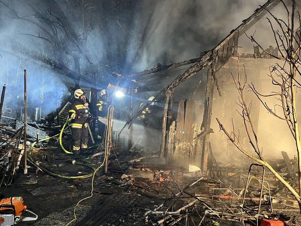 Mehrere Feuerwehrleute bekämpfen in der Nacht einen Brand in einem schwer beschädigten Gebäude. Dichte Rauchschwaden sind sichtbar.