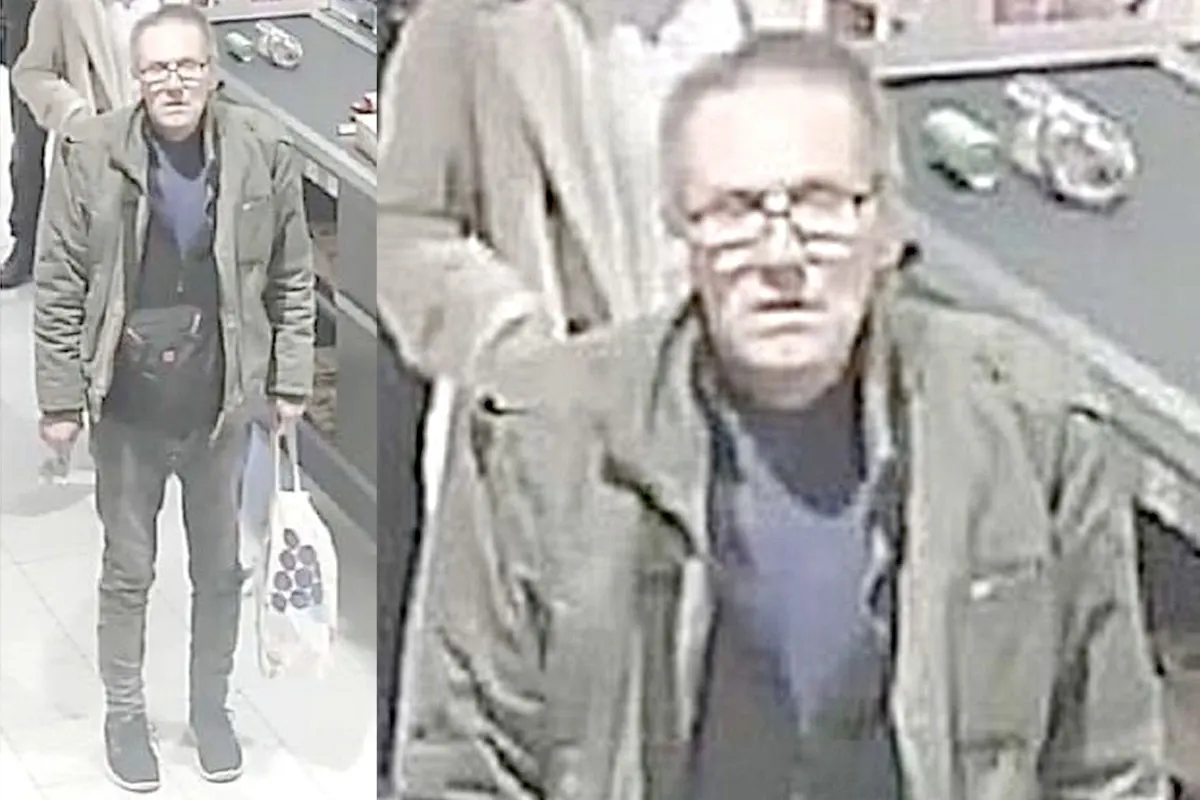 Ein Mann mit Brille und Winterjacke steht an einem Kassenschalter in einem Supermarkt. Er hält eine Einkaufstasche.