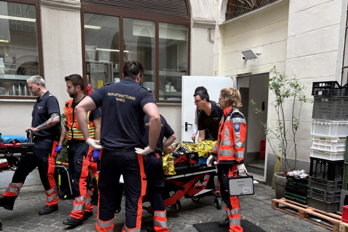 Mehrere Rettungskräfte der Berufsrettung Wien befinden sich in einem Innenhof und transportieren eine Person auf einer Bahre. Ein Mitarbeiter trägt einen Koffer, während eine andere Person die Bahre schiebt.