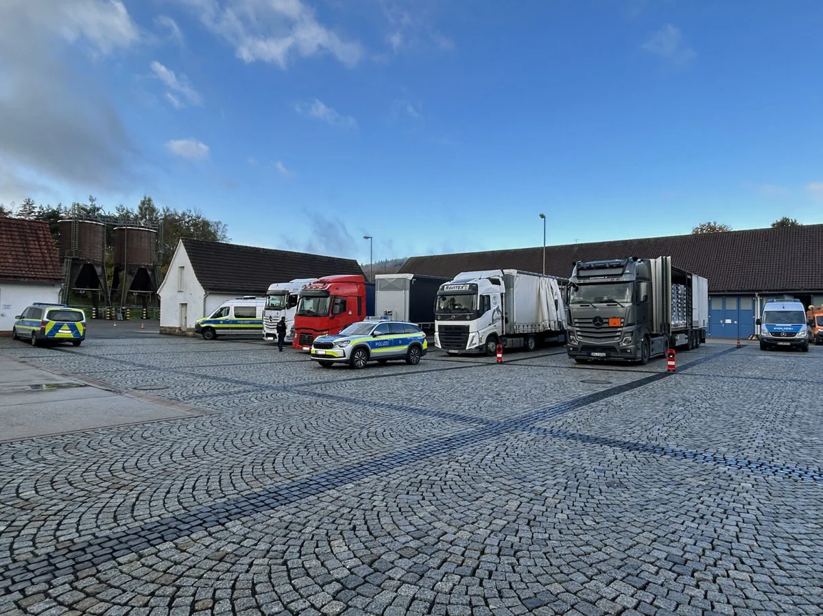 Auf einem gepflasterten Hof stehen mehrere Lastwagen neben Polizeifahrzeugen. Es sind blaue und weiße Lkw zu sehen.