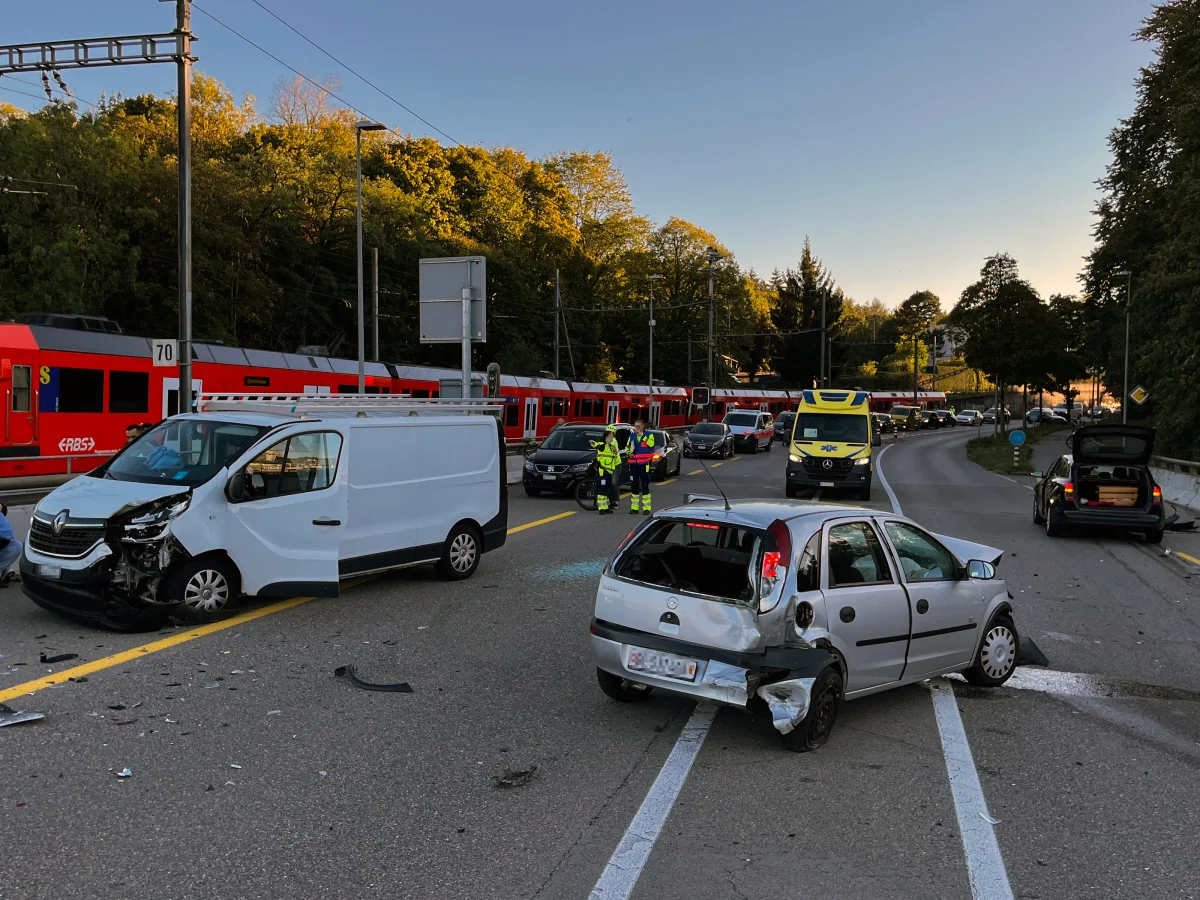 Ein Verkehrsunfall zeigt einen beschädigten weißen Van und einen silbernen Kleinwagen auf einer Straße. Rettungskräfte befinden sich in der Nähe des Unfallortes.