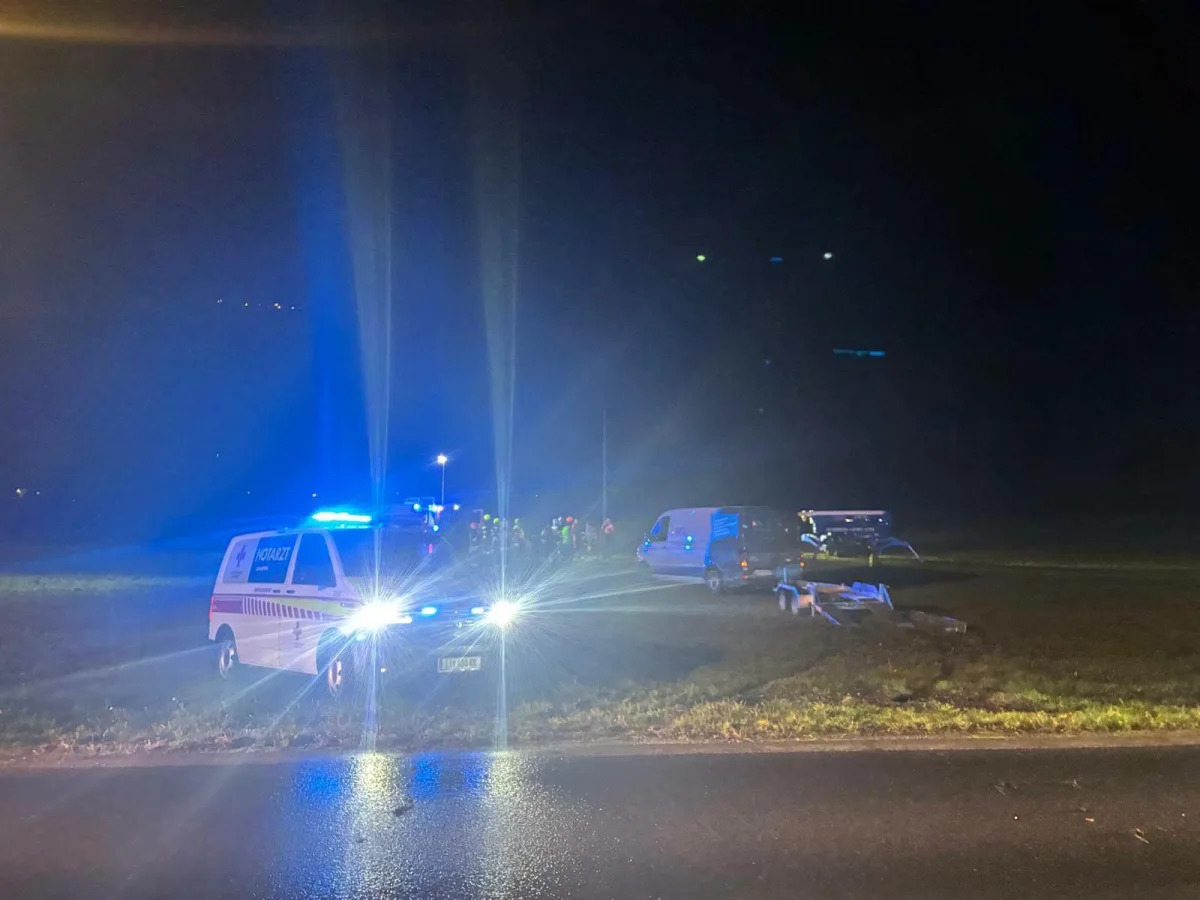 Ein Rettungswagen mit eingeschaltetem Blaulicht steht bei Nacht auf einer Landstraße. Im Hintergrund ist ein weiteres Fahrzeug sichtbar.