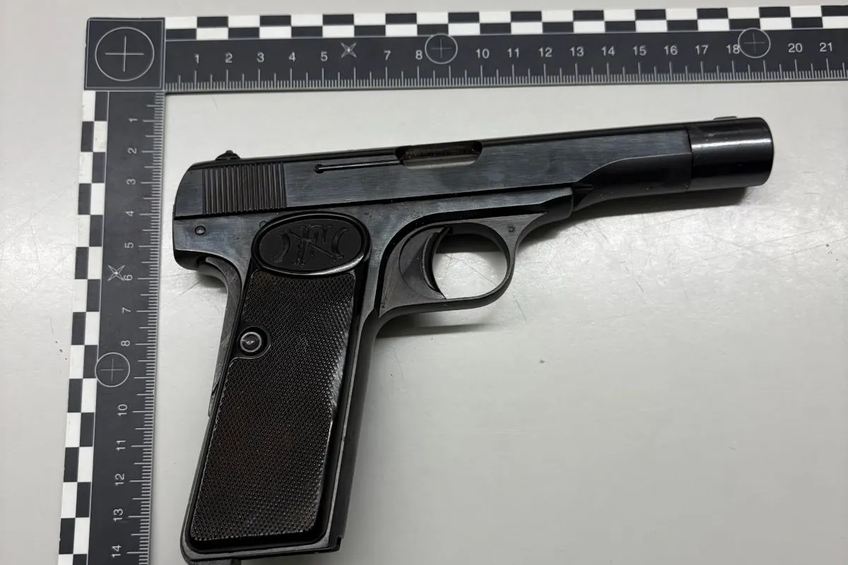 Nahaufnahme einer schwarzen Pistole, die neben einem Maßband zur Kriminaltechnik auf einem weißen Tisch liegt. Die Pistole zeigt das Logo FN auf dem Griff.