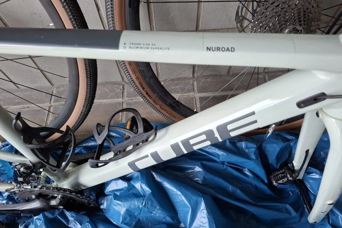 Ein helles Fahrrad der Marke CUBE liegt auf einer blauen Plane. Der Rahmen ist deutlich sichtbar und zeigt die Aufschrift 'NUROAD'.