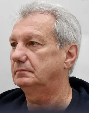 Ein älterer Mann mit grauen Haaren, der zur Seite schaut, vor einem neutralen Hintergrund.