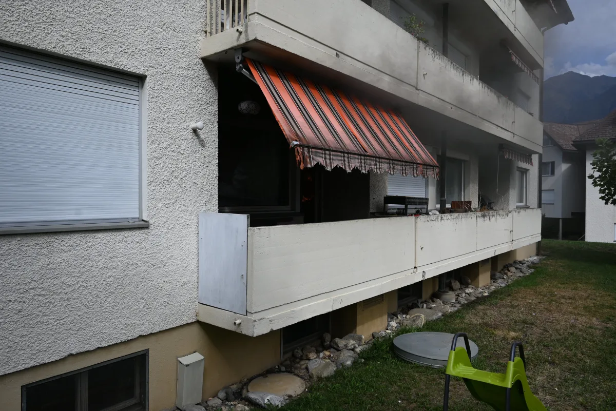 Ein Wohngebäude mit einem Balkon, von dem Rauch aufsteigt. Der Balkon hat eine gestreifte Markise.