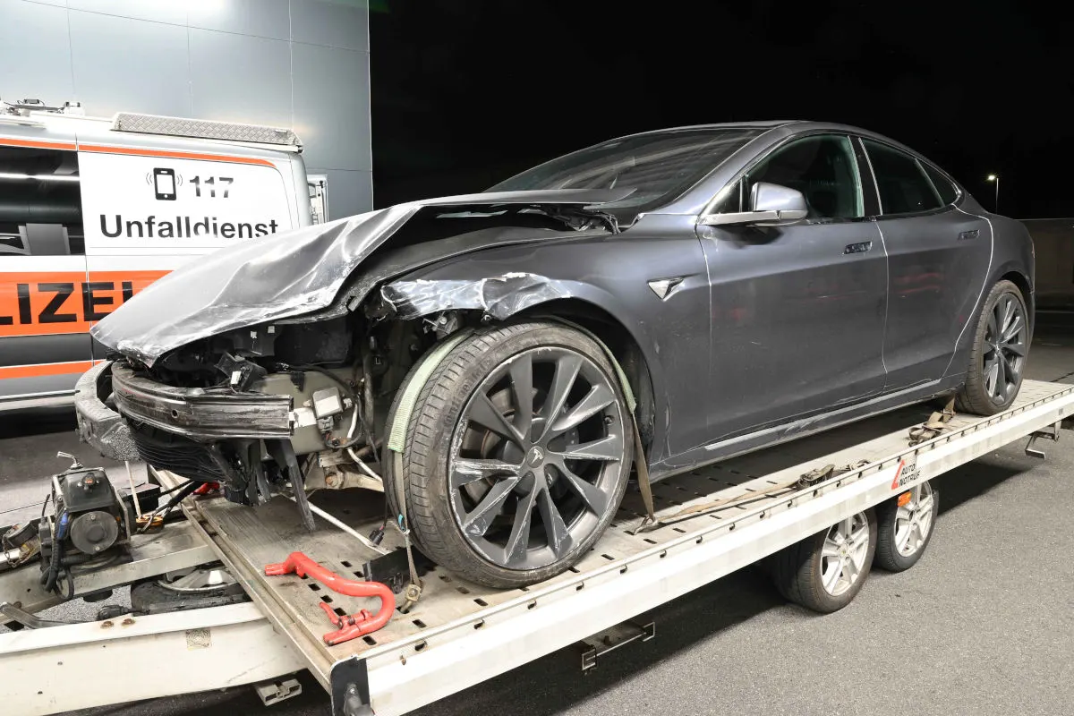 Ein Tesla mit sichtbaren Frontschäden steht auf einem Abschleppwagen. Im Hintergrund ist ein Fahrzeug des Polizeidienstes sichtbar.