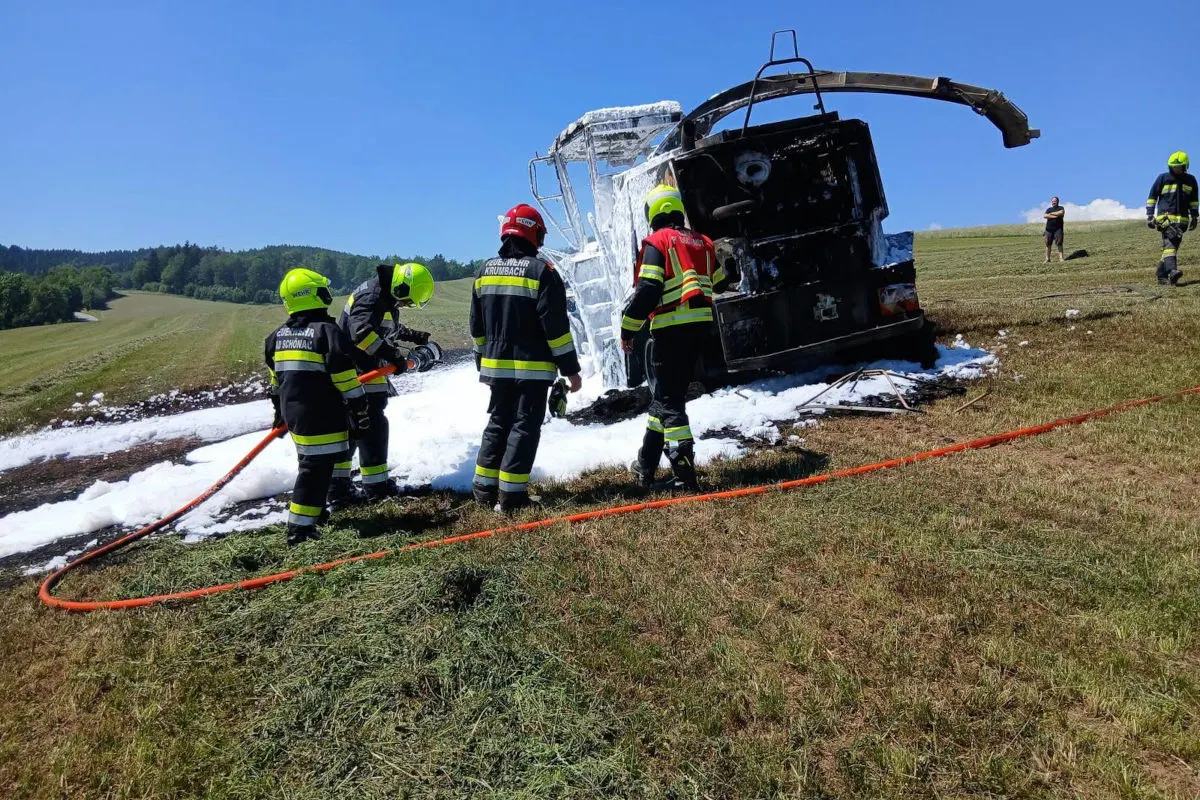 Eine Gruppe von Feuerwehrleuten in Schutzkleidung löscht einen brennenden Lastwagen auf einem grasbewachsenen Feld.