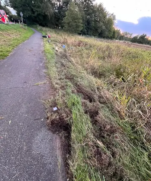 Ein schmaler Weg verläuft entlang eines Feldes mit sichtbar umgeknicktem Gras, das auf einen Unfall hindeutet.