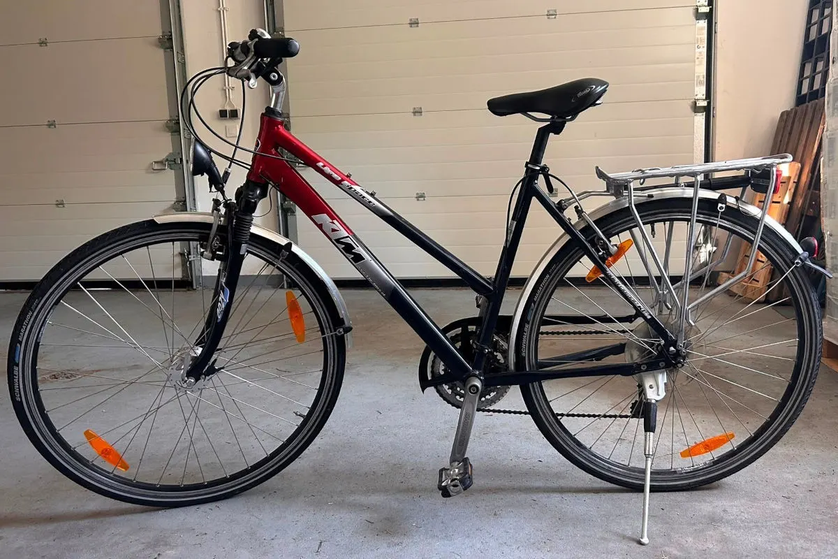 Ein rot-schwarzes Fahrrad steht seitlich in einer offenen Garage. Es hat Reflektoren an den Rädern und einen Gepäckträger.