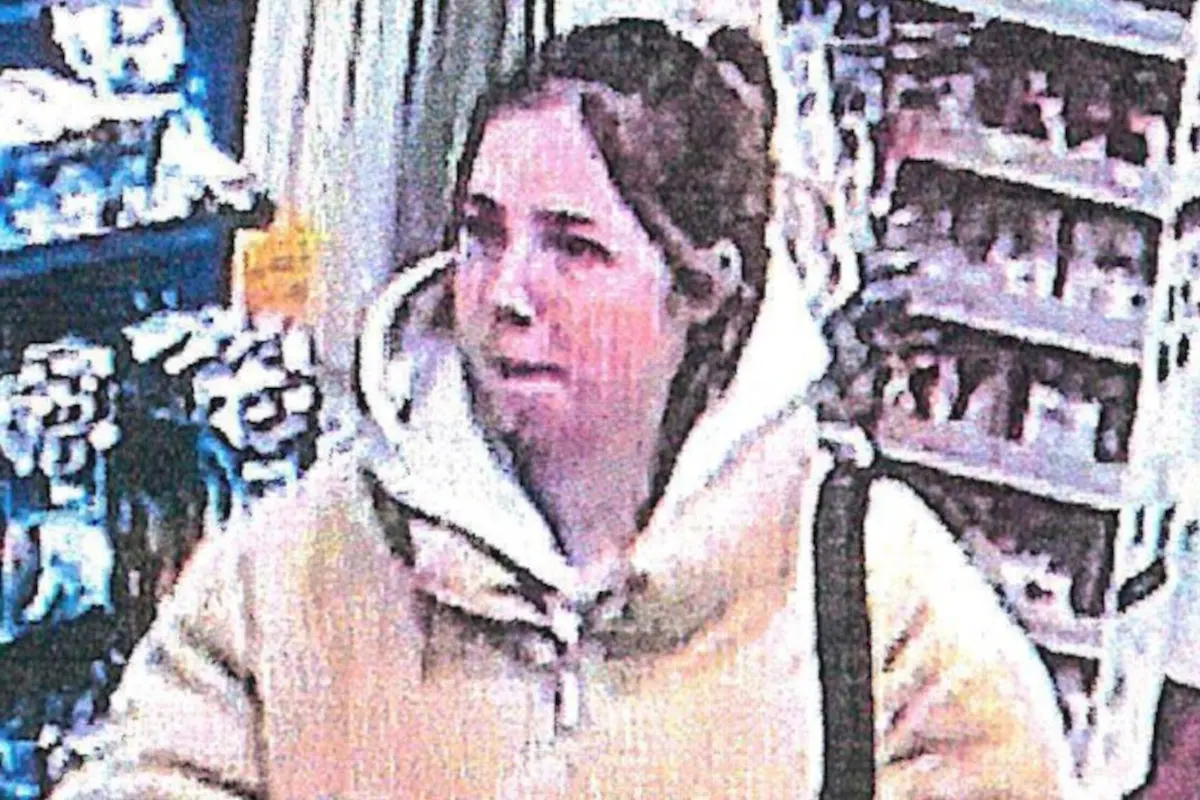Eine Frau mit heller Jacke wird in einem Geschäft von einer Überwachungskamera erfasst. Im Hintergrund sind Regale sichtbar.