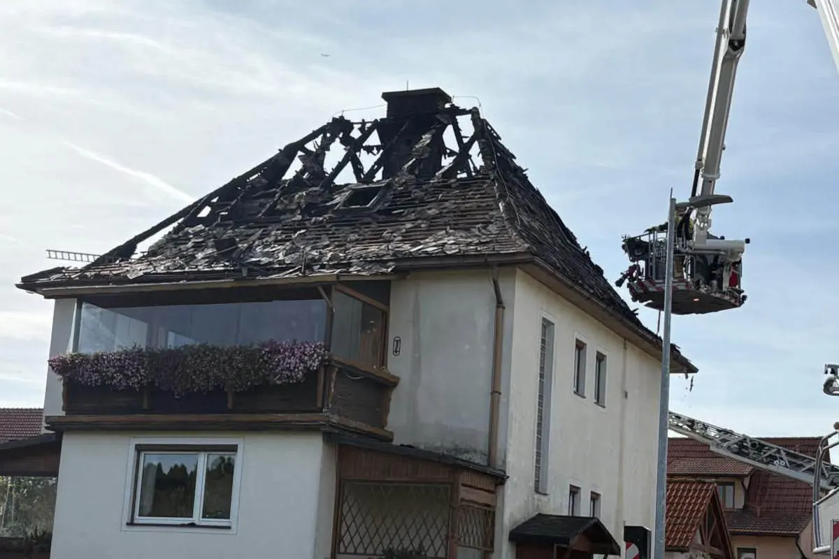Ein Haus mit einem durch Feuer zerstörten Dach. Eine Feuerwehrleiter ist an der Fassade eingesetzte, um den Schaden zu begutachten.