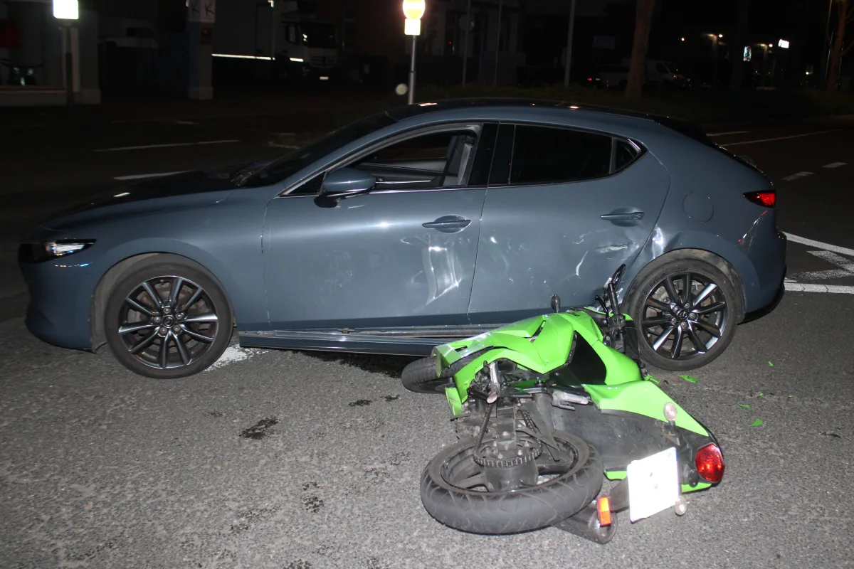 Ein graues Auto hat bei Nacht mit einem grünen Motorrad auf der Straße kollidiert. Das Motorrad liegt umgestürzt vor dem Auto.