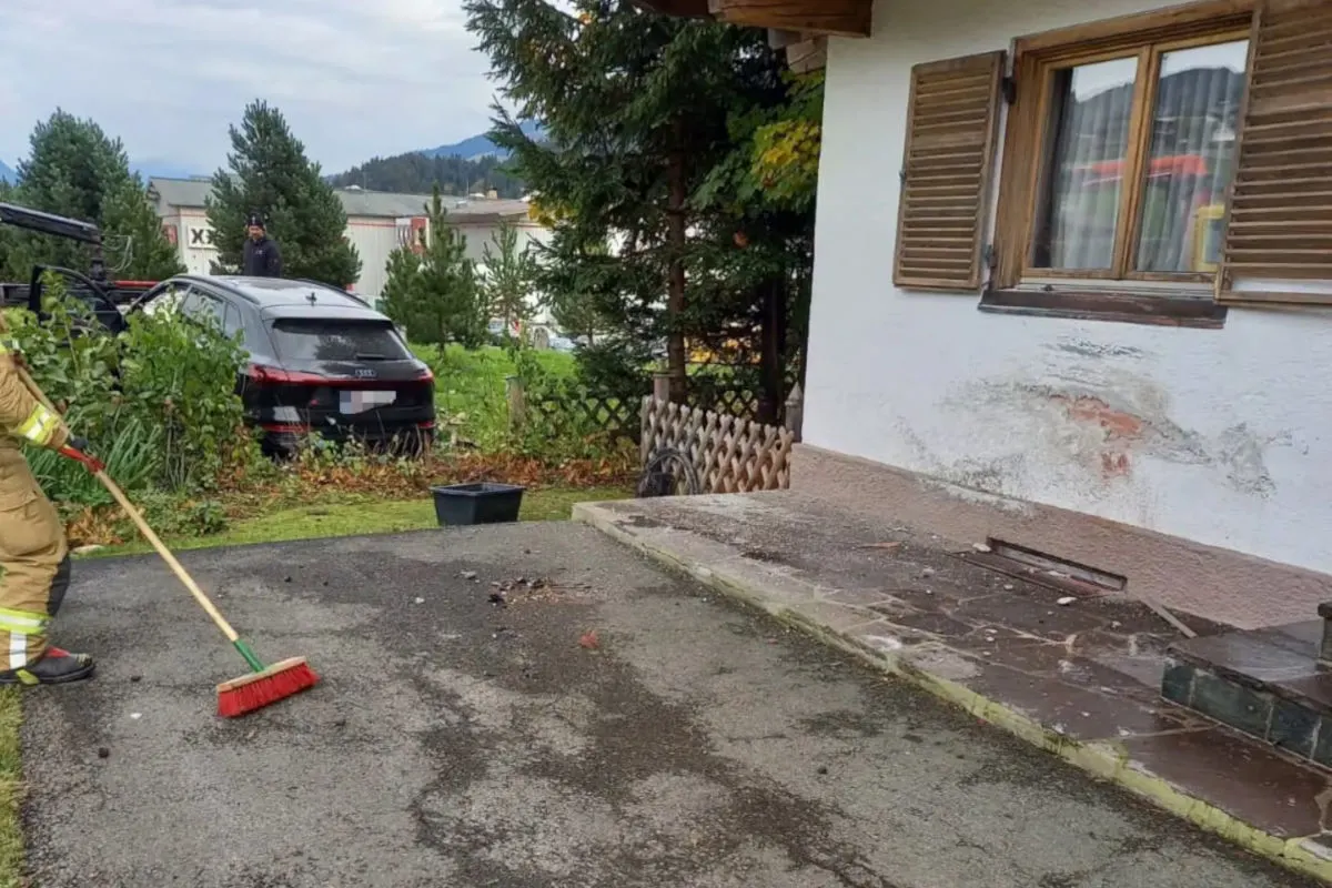 Ein Feuerwehrmann kehrt Schutt vor einem Haus mit einer beschädigten Wand. Im Hintergrund ist ein Fahrzeug teilweise in einem Garten zu sehen.