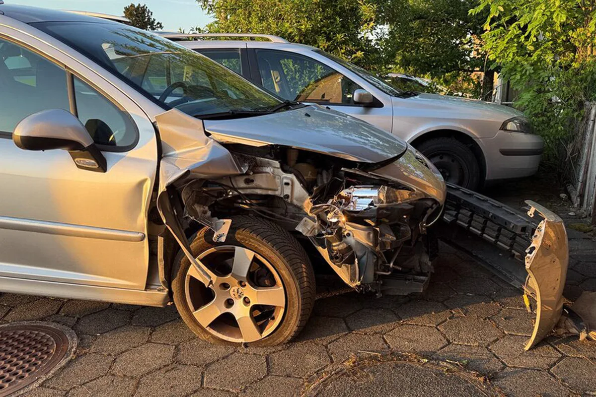Ein silbernes Auto mit erheblichem Frontschaden und abnehmender Stoßstange, daneben steht ein weiteres Auto. Die Szene wirkt ruhig und zeigt keinen sichtbaren Polizeieinsatz.