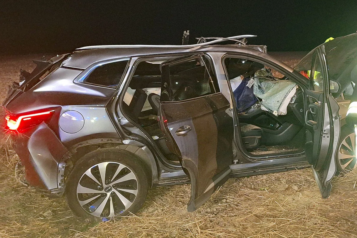 Ein silbernes Fahrzeug steht stark beschädigt in einem Feld. Die Türen sind offen, und die Airbags im Inneren sind ausgelöst.
