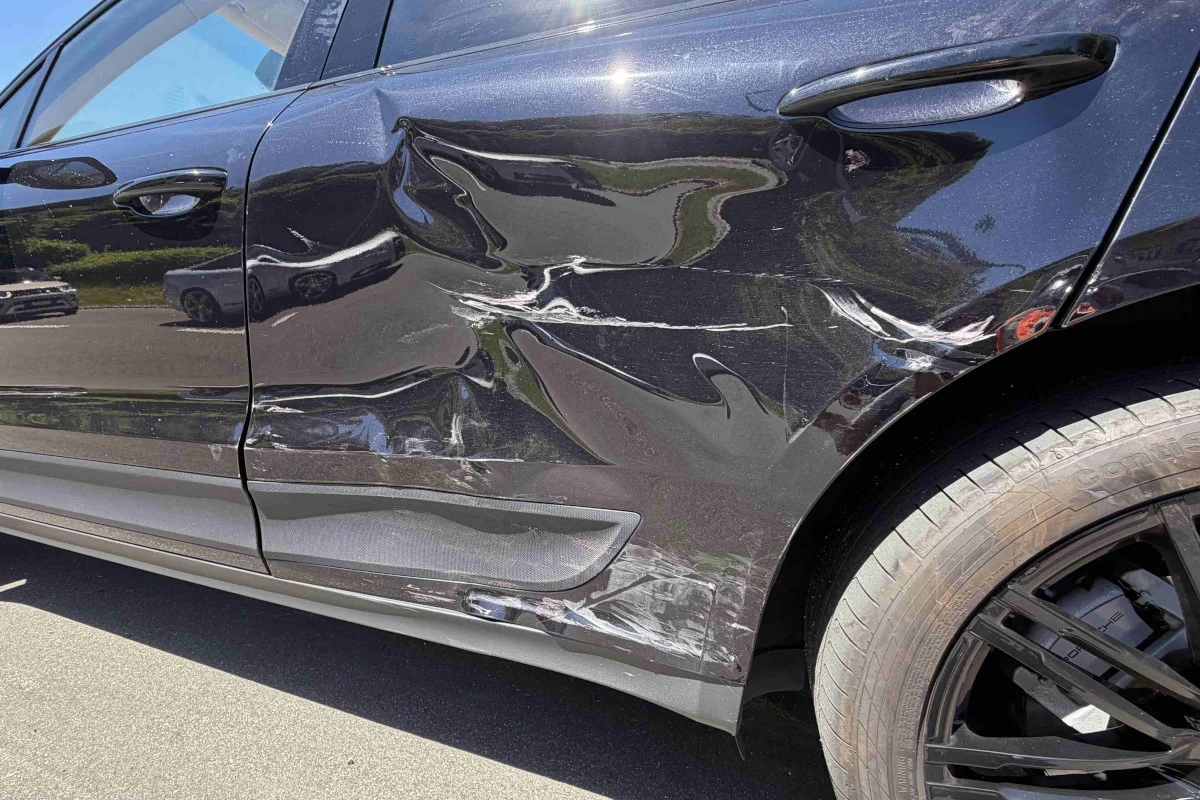 Ein schwarzes Auto zeigt schwere Schäden an der rechten Seite, inklusive Dellen und Kratzspuren, vermutlich von einem Unfall.