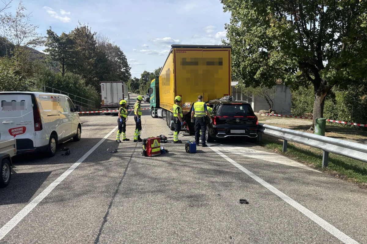 Mehrere Polizeibeamte stehen auf einer Straße; ein schwarzes Auto ist hinten auf einen gelben Lkw aufgefahren. Rettungsausrüstung liegt auf der Fahrbahn.