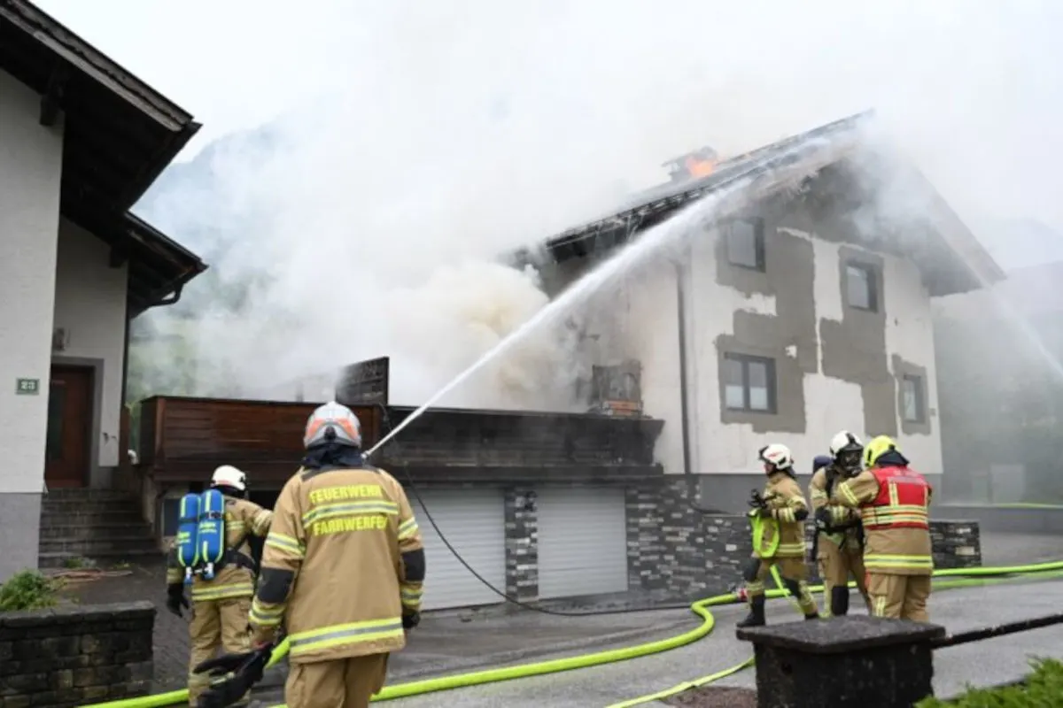 Mehrere Feuerwehrleute in kompletter Ausrüstung stehen vor einem verqualmten Wohnhaus und löschen den Brand mit Wasserschläuchen.