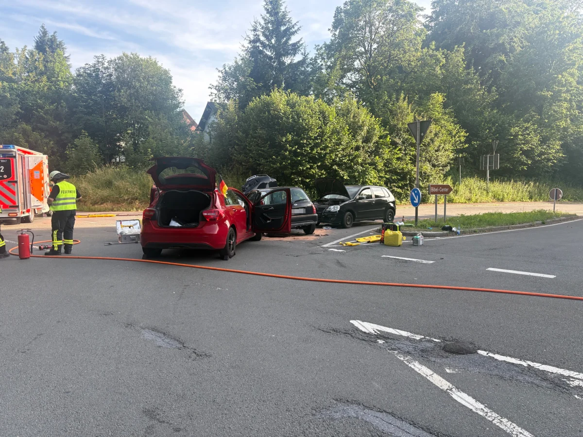 Zwei Fahrzeuge stehen mit Schäden an einer Kreuzung. Feuerwehrpersonal ist vor Ort, Absperrung und Ausrüstung sichtbar.