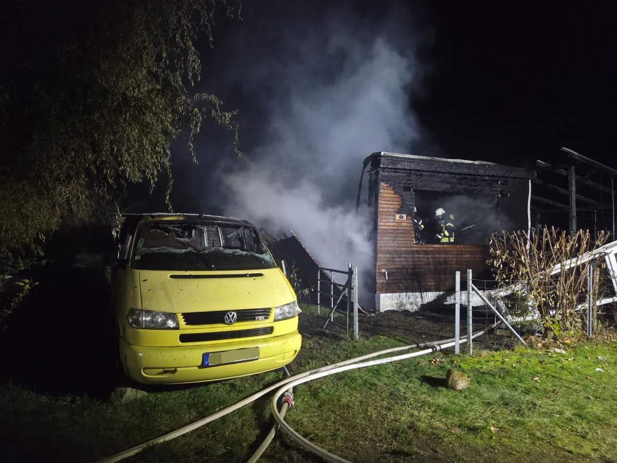 Ein gelber VW-Bus steht neben einem brennenden Gebäude. Ein Feuerwehrmann ist im Rauch sichtbar und löscht das Feuer.