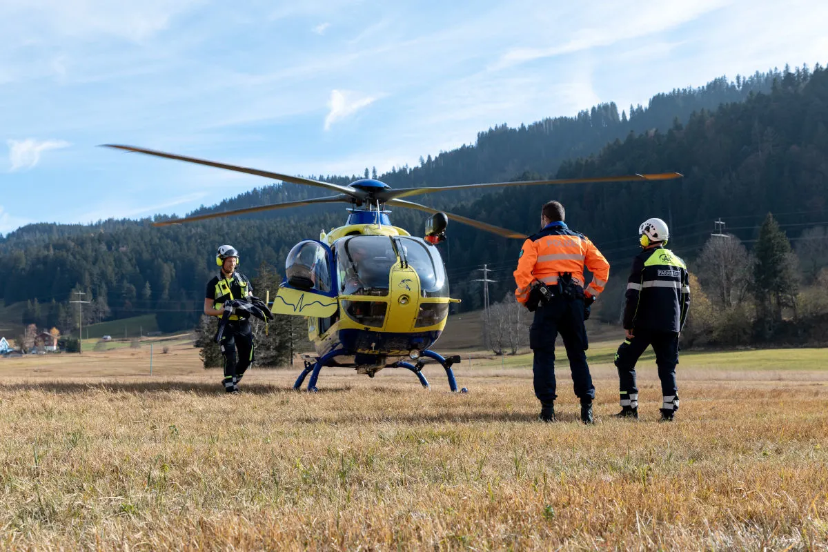Ein gelb-blauer Polizeihelikopter steht auf einem Feld, umgeben von mehreren Einsatzkräften in Schutzkleidung.