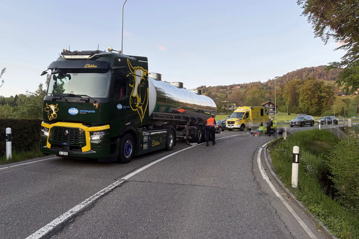 Auf einer Landstraße steht ein grüner Tanklaster mit einem großen Kuh-Motiv. Daneben ist ein gelber Rettungswagen geparkt.