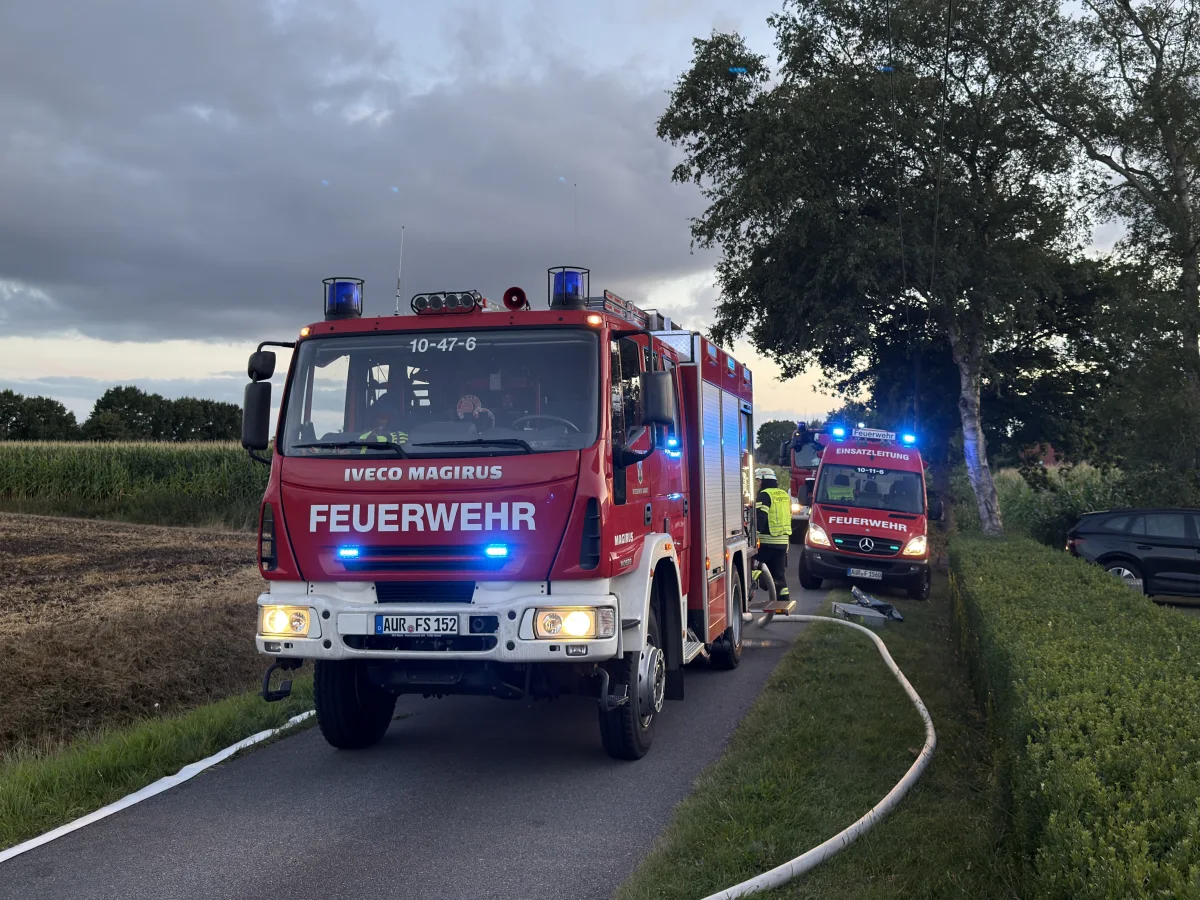Zwei Feuerwehrfahrzeuge, ein Iveco Magirus und ein Einsatzleitungsfahrzeug, stehen mit eingeschaltetem Blaulicht auf einer ländlichen Straße.