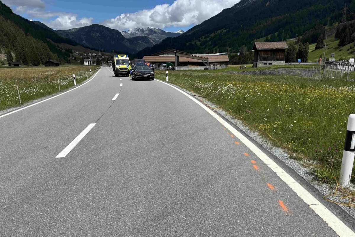 Auf einer alpinen Landstraße stehen links ein Ambulanzfahrzeug und daneben ein Pkw. Umgeben von Wiesen und Bergen im Hintergrund.
