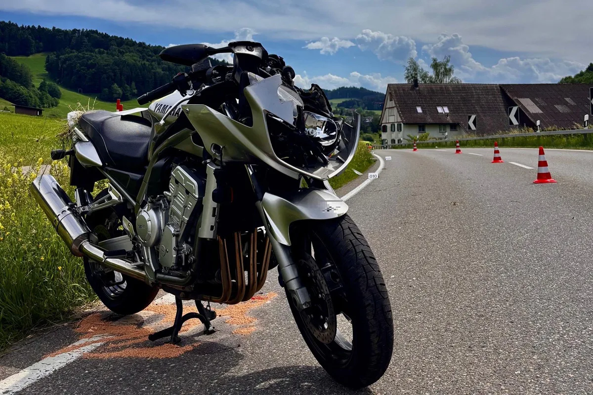 Ein verunfalltes Motorrad steht angeschlagen auf einer Landstraße. Leitkegel sind in der Nähe zur Absicherung aufgestellt.