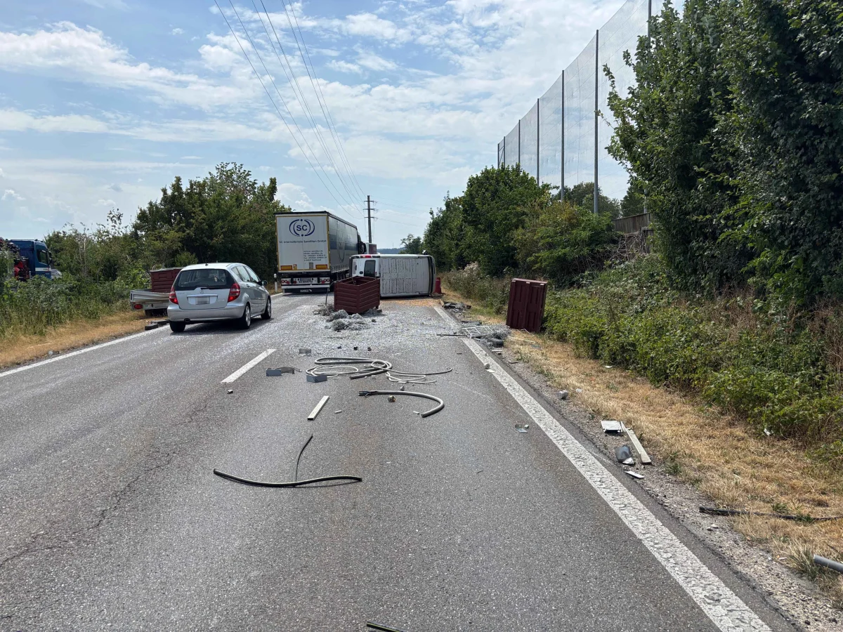 Ein umgekippter Lkw liegt quer über der Landstraße. Trümmer und abgefallene Teile sind auf der Fahrbahn verstreut, mit anderen Fahrzeugen im Hintergrund.