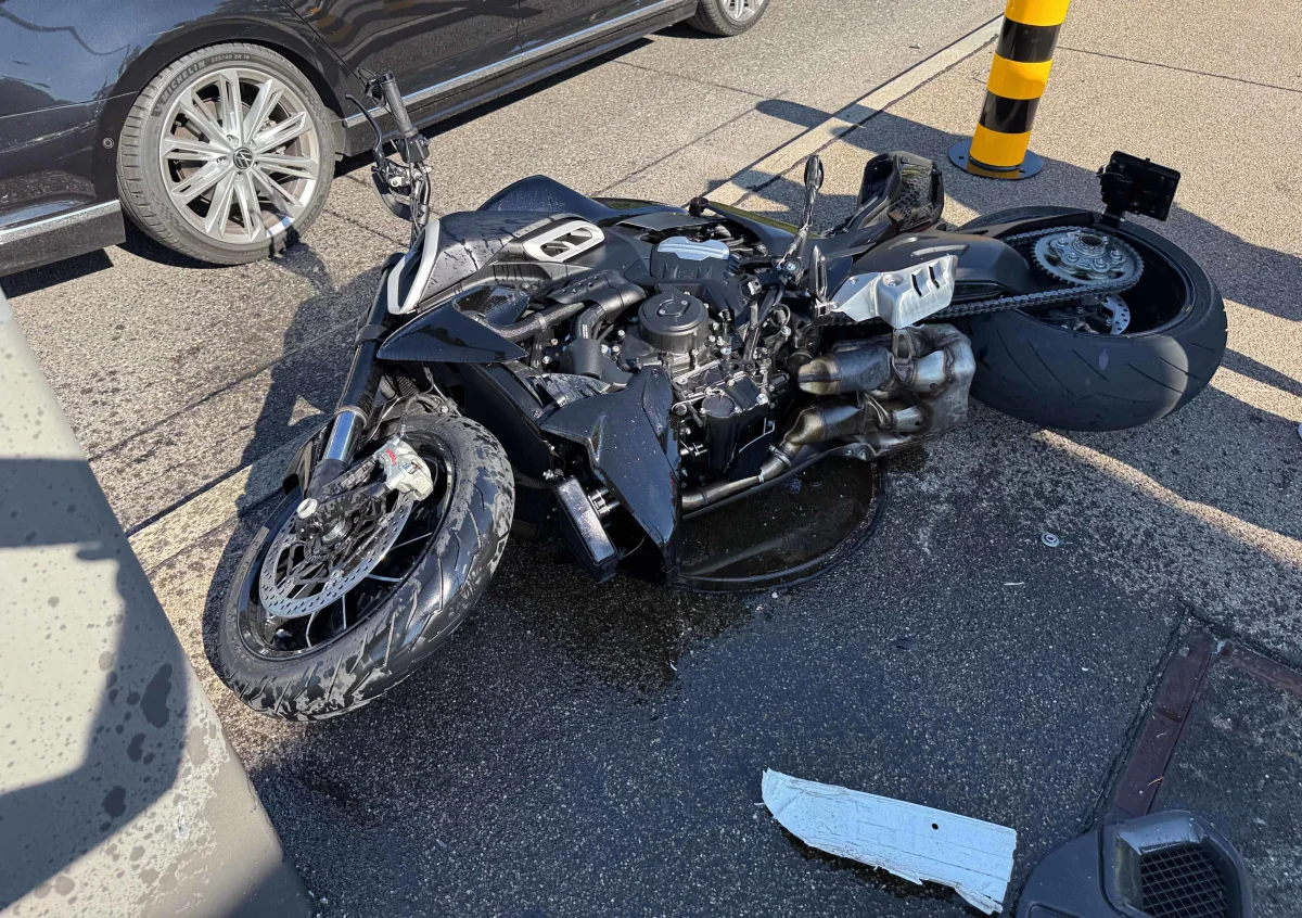 Ein schwarzes Motorrad liegt umgestürzt auf der Straße neben einem schwarzen Pkw. Es ist tagsüber, die Straße ist trocken.