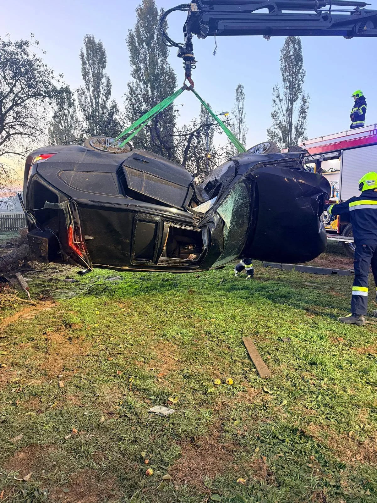 Ein schwarzes Auto wird von einem Kran aus einem Straßengraben gehoben. Mehrere Einsatzkräfte sind vor Ort zu sehen.
