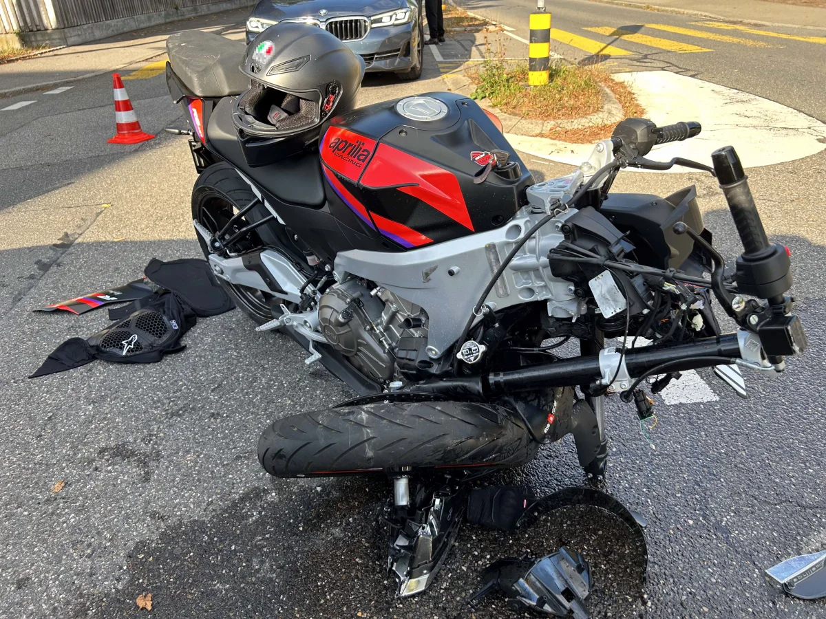 Ein stark beschädigtes Aprilia-Motorrad liegt auf einem Asphaltweg. Teile und ein Helm sind verstreut.