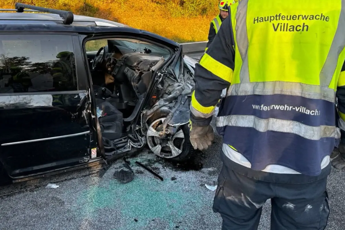 Ein Feuerwehrmann in einer Warnweste steht neben einem stark beschädigten Auto auf einer Straße.