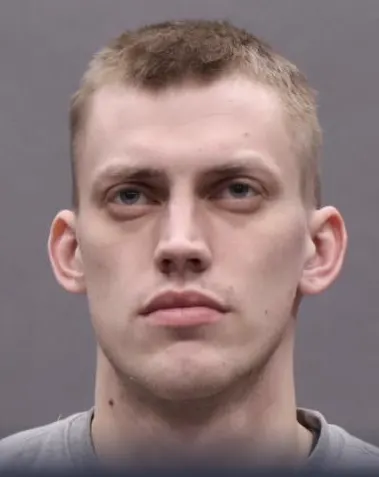 Das Bild zeigt das Gesicht eines jungen Mannes mit kurzem, hellem Haar, der direkt in die Kamera schaut.