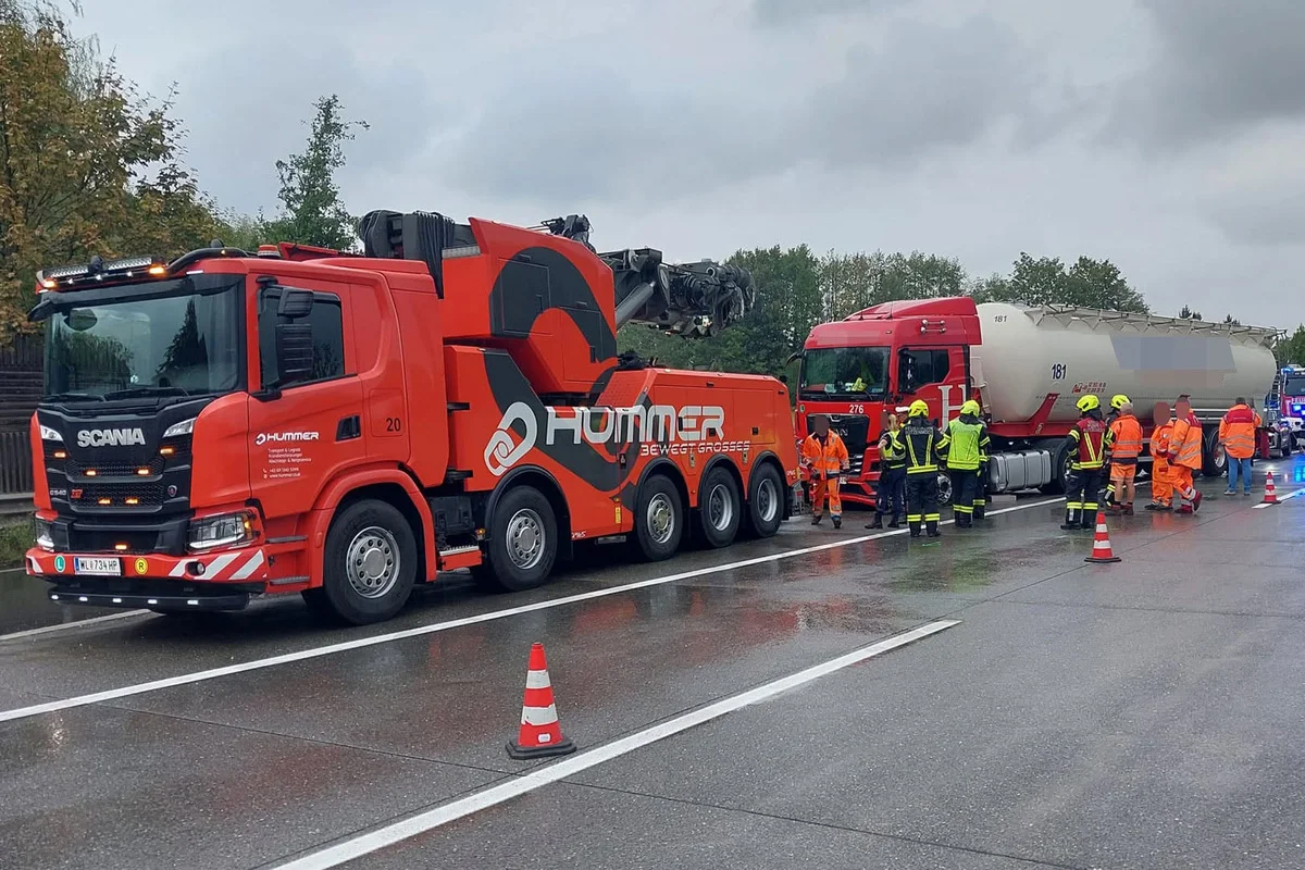 Ein großer roter Abschleppwagen neben einem verunfallten Lkw auf der Autobahn, umgeben von Rettungskräften in Schutzkleidung.