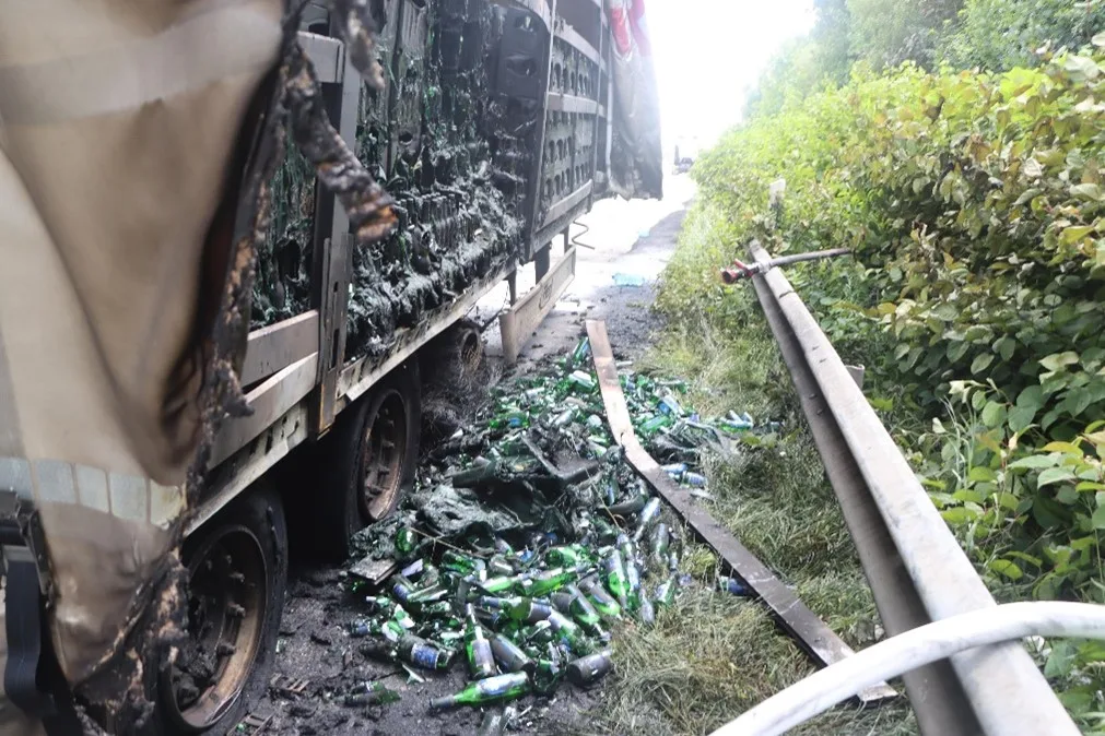 Ein beschädigter Lkw hat seine Ladung verloren, kaputte Flaschen liegen verstreut auf der Straße. Der Lkw zeigt deutliche Anzeichen von Schaden.