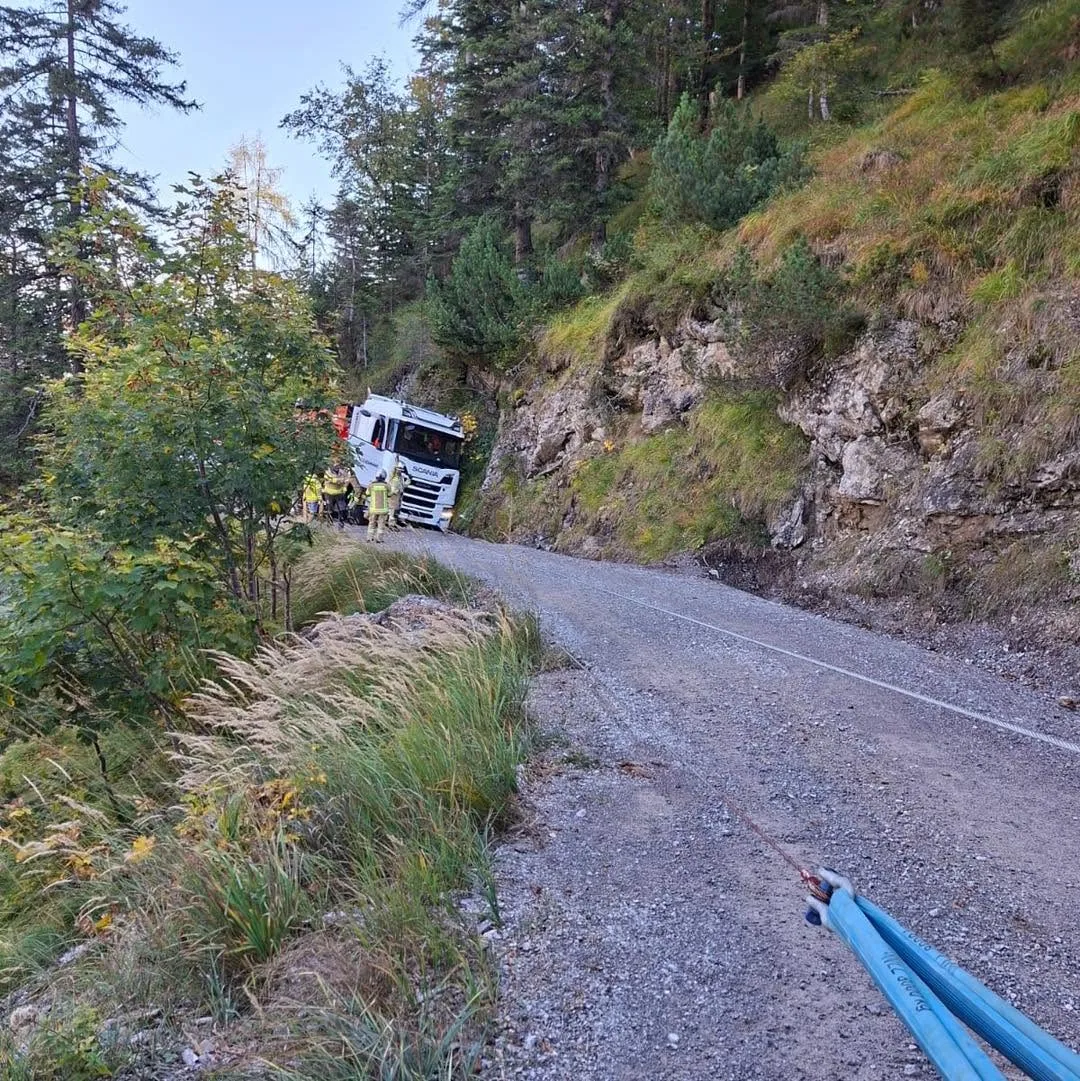 Ein weißer Lastwagen ist von einer schmalen Bergstraße abgekommen und steckt seitlich im Hang fest. Mehrere Personen in Schutzanzügen sind vor Ort.