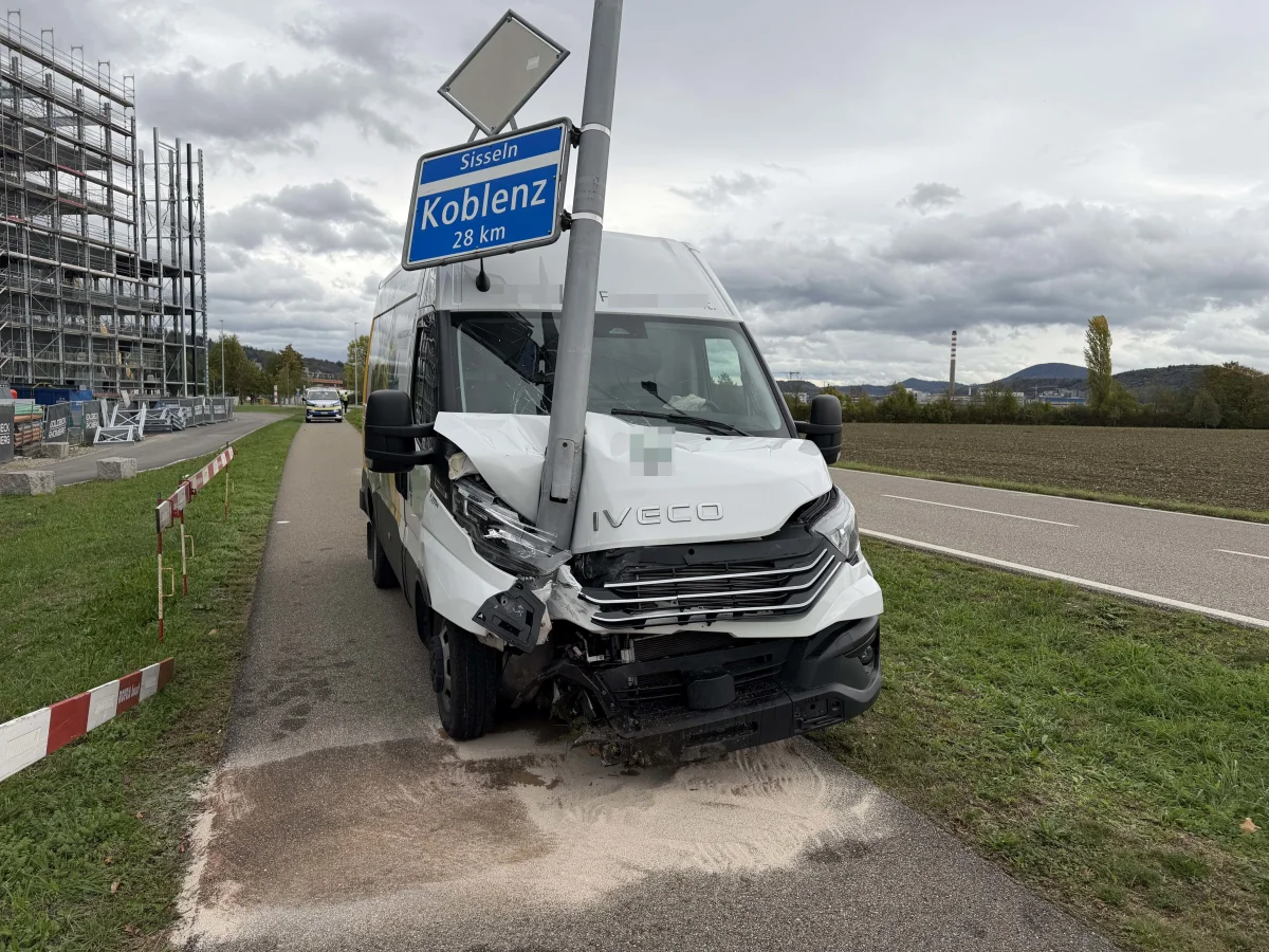Ein weißer Transporter ist frontal gegen ein Verkehrsschild geprallt, das Schild ist verbogen. Im Hintergrund sind Wolken am Himmel.