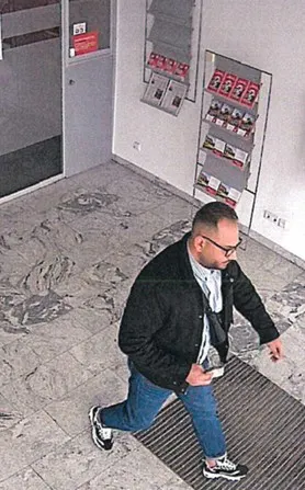 Ein Mann mit Brille und Jacke betritt einen hellen Raum. Im Hintergrund sind Informationsständer und eine Tür zu sehen.