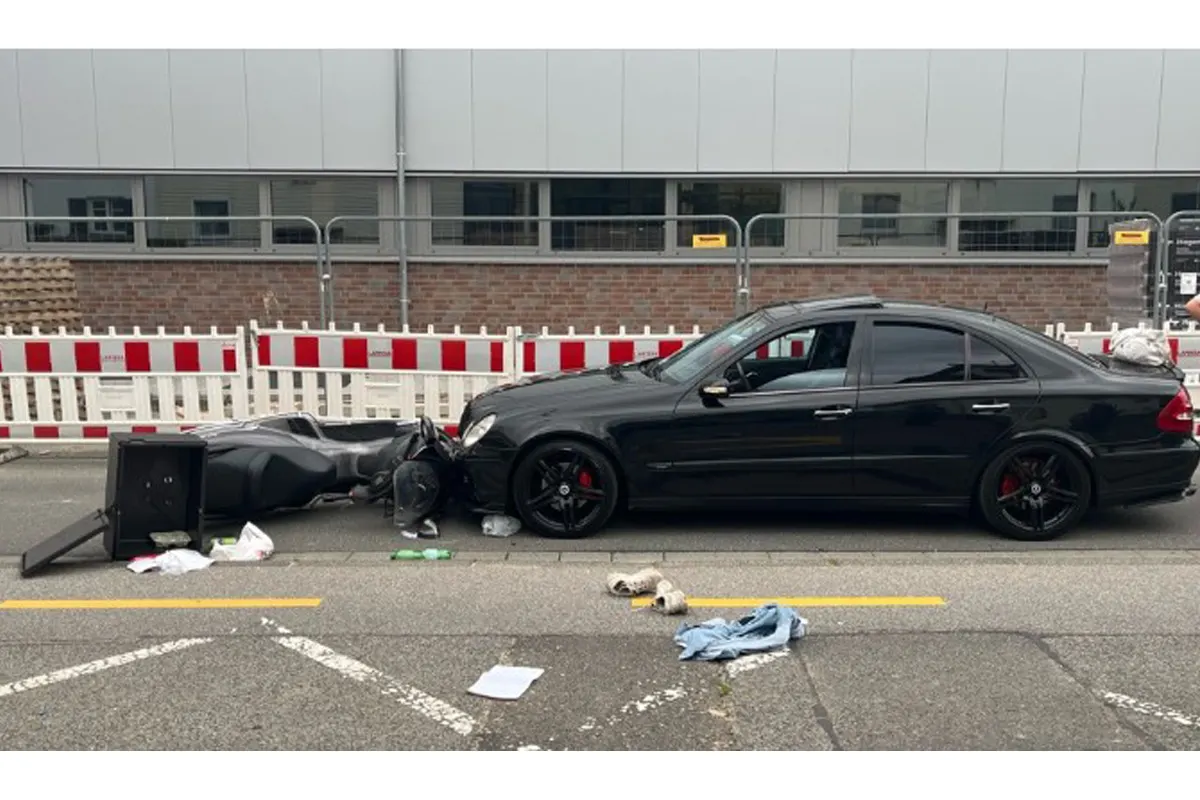 Ein schwarzer Mercedes ist auf einer städtischen Straße mit einem Roller kollidiert. Auf der Straße liegen verstreute Gegenstände.